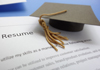 A college mortar board hat laying on top of a resume.