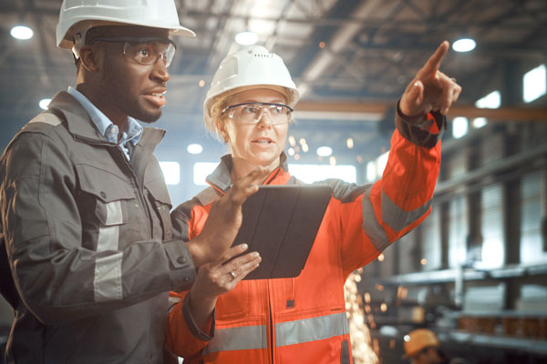 Image of a Black man and a white woman wearing hardhats at a construction site.